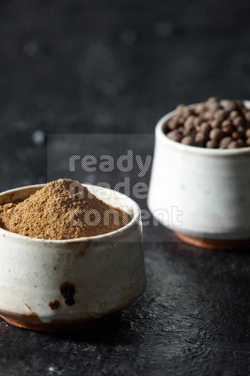 وعاءان بيج، أحدهما ممتلئ ببودرة بهار الفلفل الحلو والآخر بالحبوب على خلفية سوداء