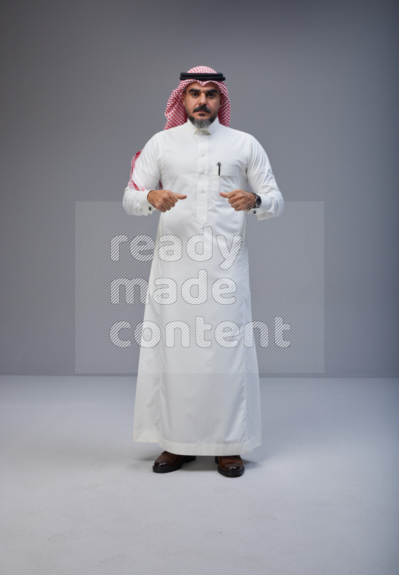 Saudi man Wearing Thob and red white Shomag standing interacting with the camera on Gray background
