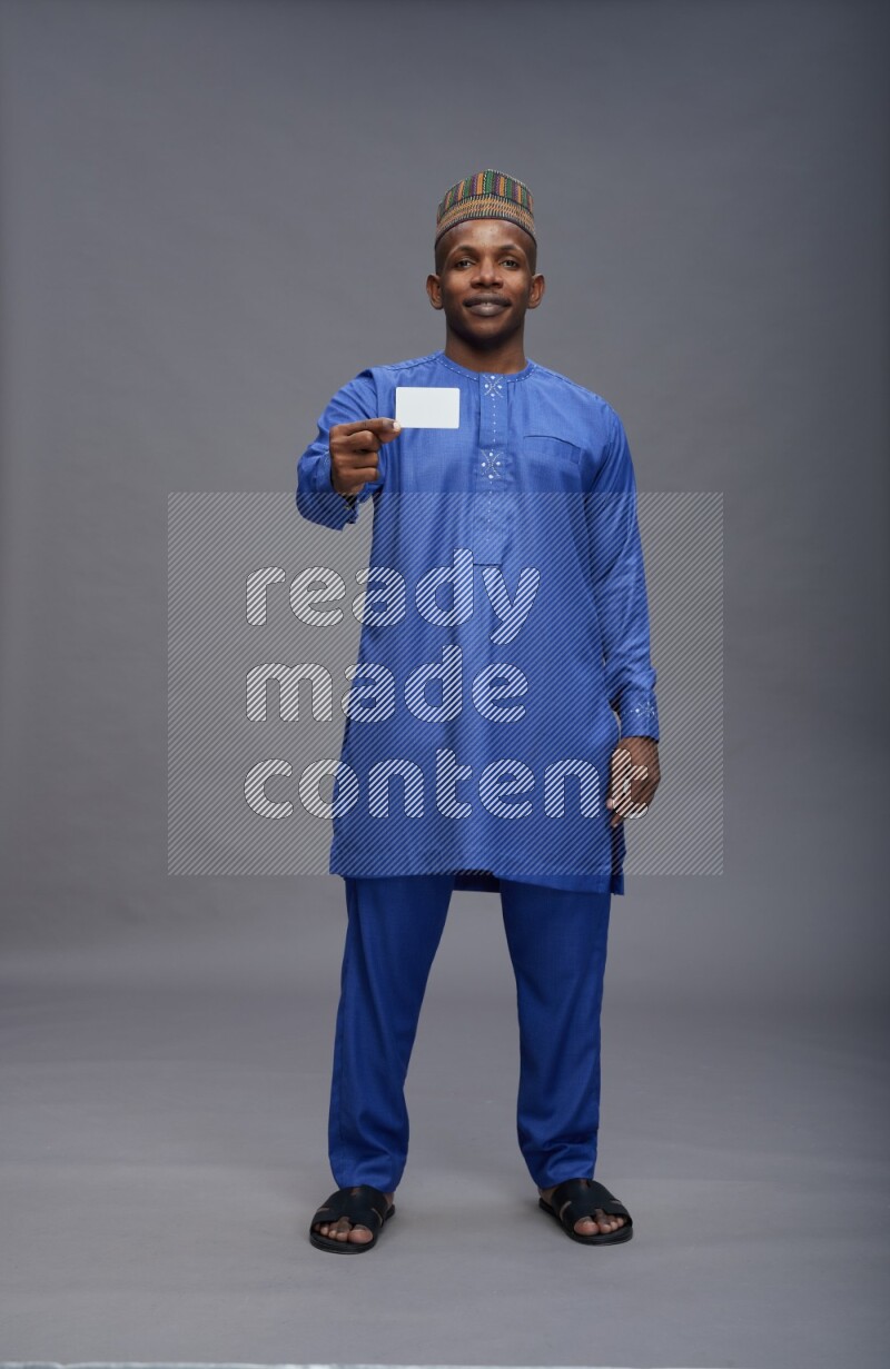 Man wearing Nigerian outfit standing holding ATM card on gray background