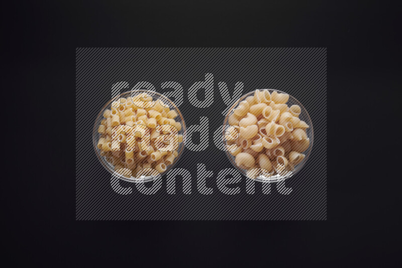 Different pasta types in glass bowls on black background