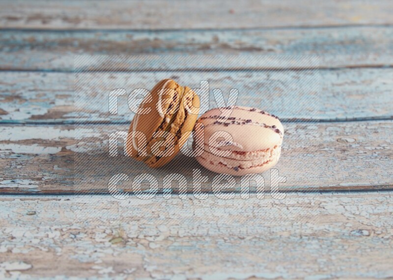 45º Shot of of two assorted Brown Irish Cream, and pink orange blossom  macarons on light blue background