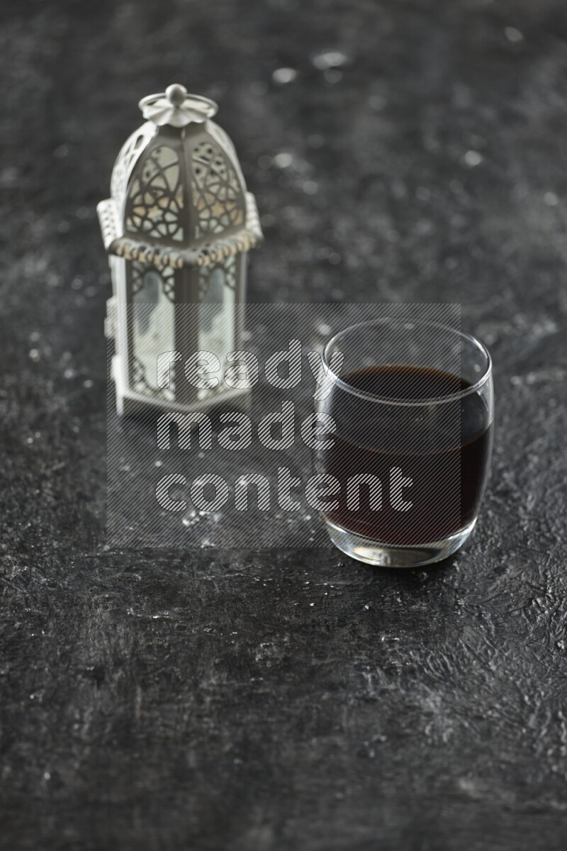 A white lantern with different drinks, dates, nuts, prayer beads and quran on textured black background