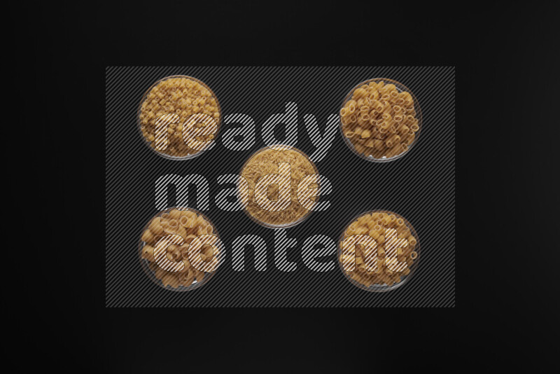Different pasta types in 5 glass bowls on black background