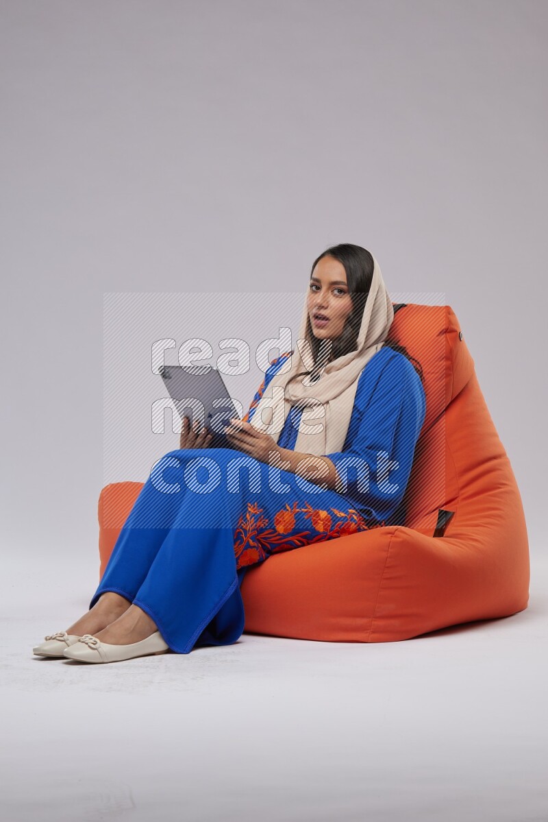 A Saudi woman sitting on an orange beanbag and working on tablet