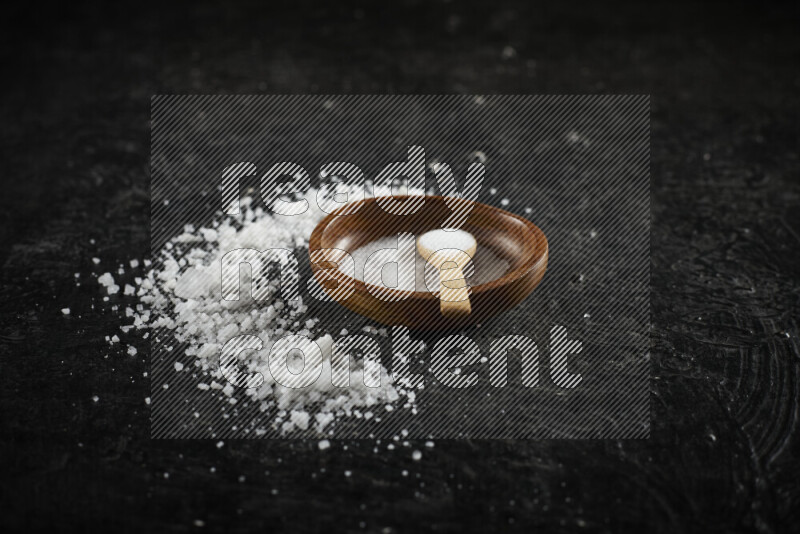 A pottery plate full of fine salt with bunch of coarse salt beside it on black background