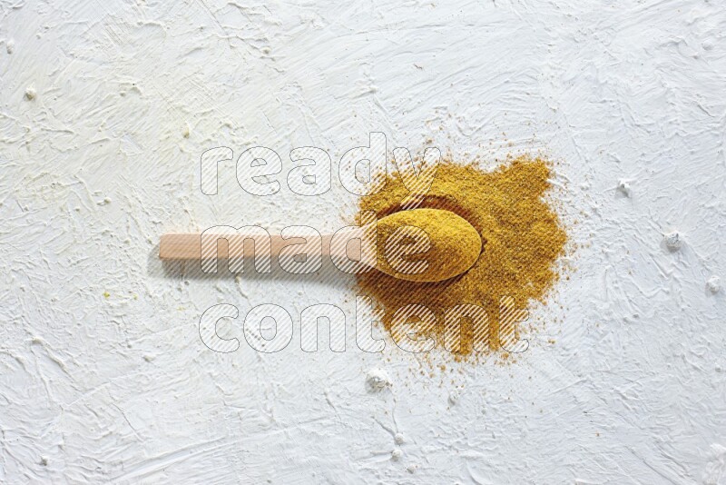 A wooden spoon full of turmeric powder on textured white background