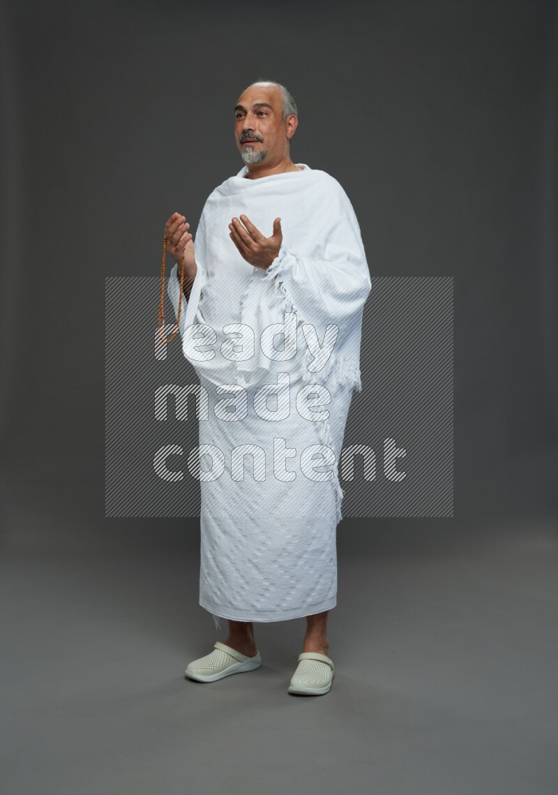 A man wearing Ehram Standing dua'a on gray background