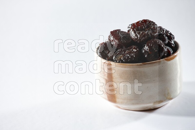 A beige ceramic bowl full of dried plums on a white background in different angles