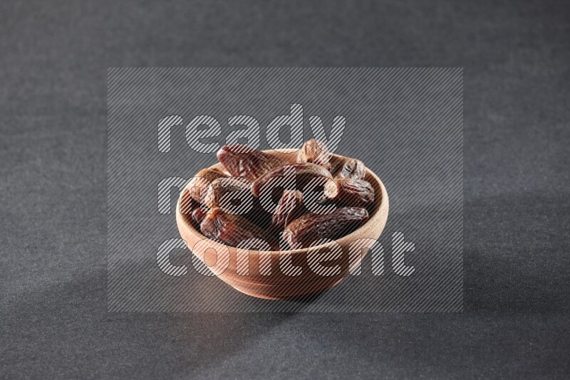 A wooden bowl full of dried dates on a black background in different angles