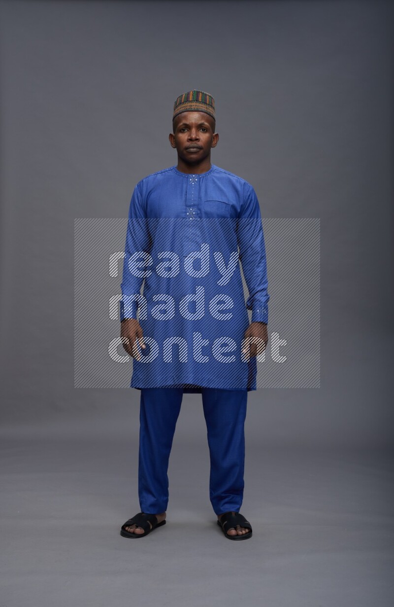 Man wearing Nigerian outfit standing interacting with the camera on gray background