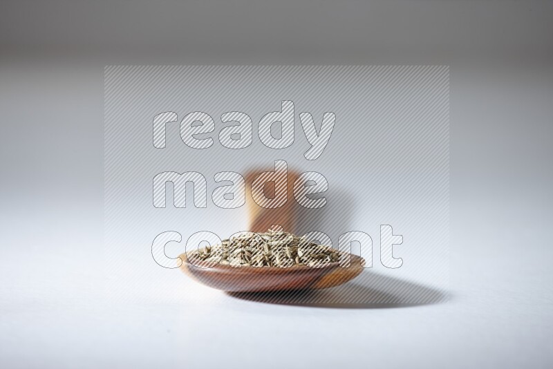 A wooden ladle full of cumin seeds on a white flooring