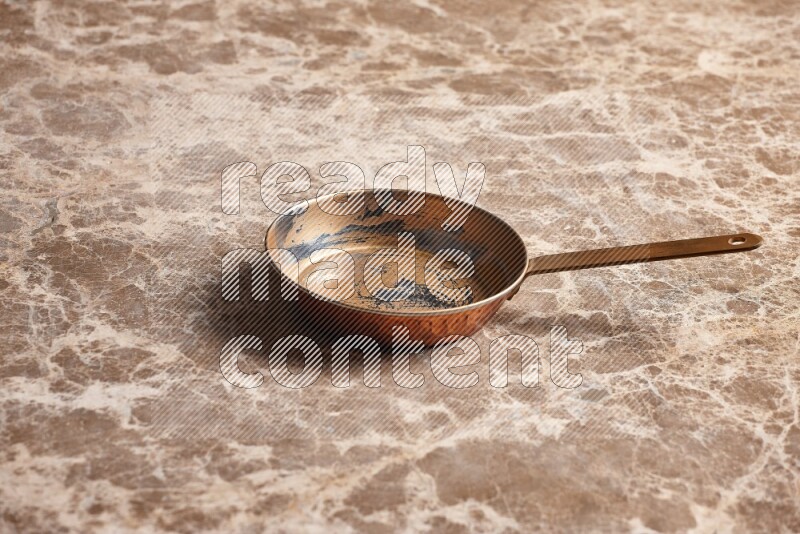A small copper pan on beige marble background