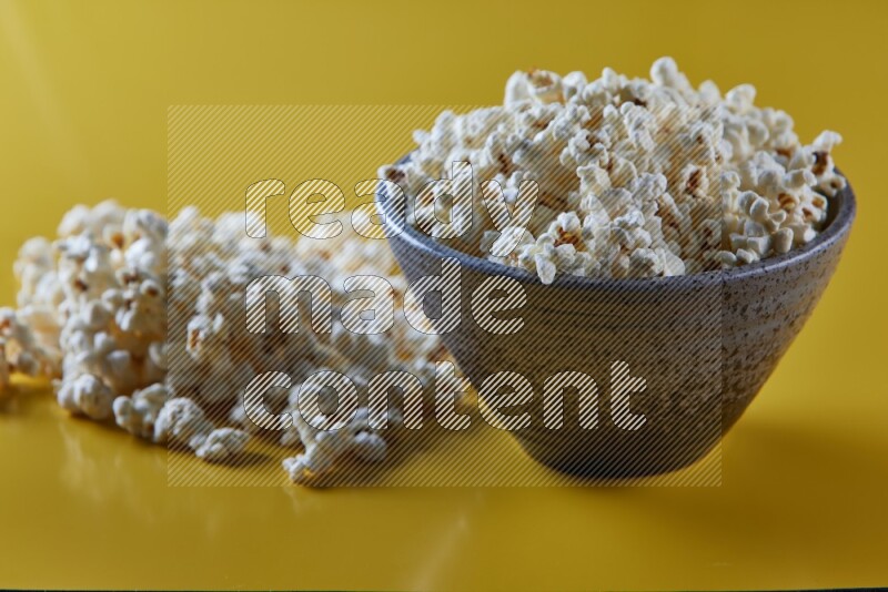 A multicolored pottery bowl full of popcorn with popcorn beside it on a yellow background in different angles
