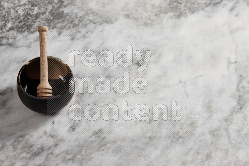Multicolored pottery bowl with wooden honey dipper in it on grey marble background