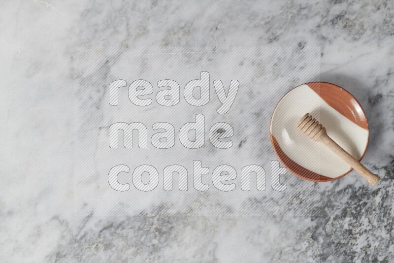 Multicolored pottery plate with wooden honey dipper in it on grey marble background