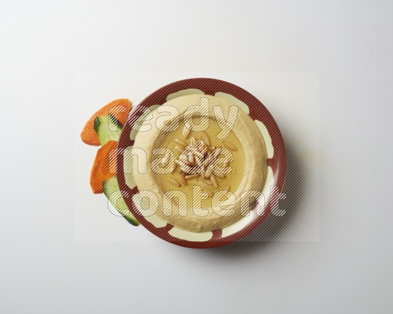 Hummus in a traditional plate garnished with pine nuts on a white background
