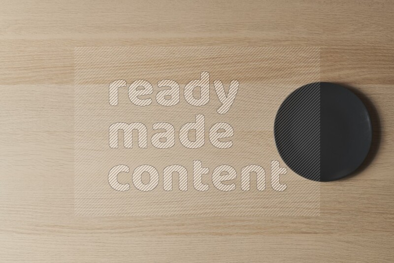 A black ceramic circular plate on light wooden background