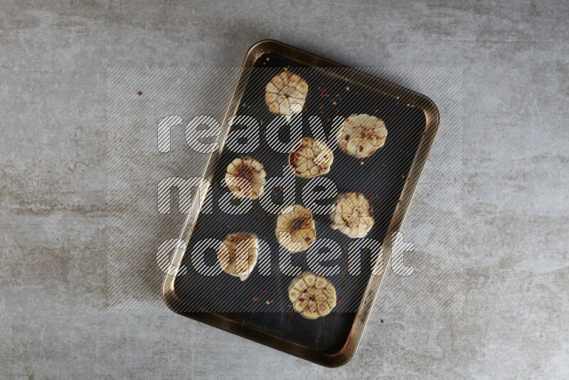 half's roasted garlic in a stainless tray on a grey textured countertop