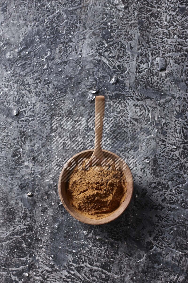 Wooden bowl full of cinnamon powder with a wooden spoon on a textured black background in different angles