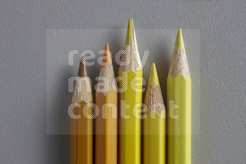 A collection of sharpened colored pencils arranged showcasing a gradient of yellow and orange hues on grey background