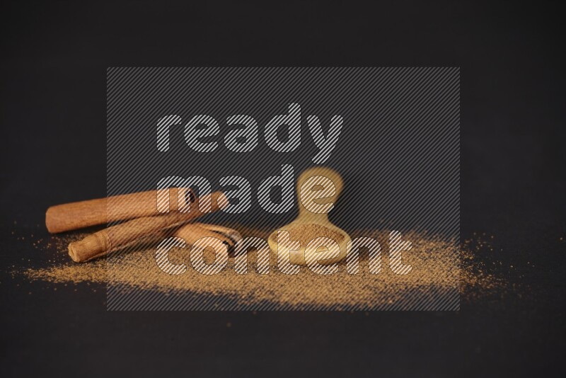Cinnamon powder in a wooden spoon and cinnamon sticks beside it on black background
