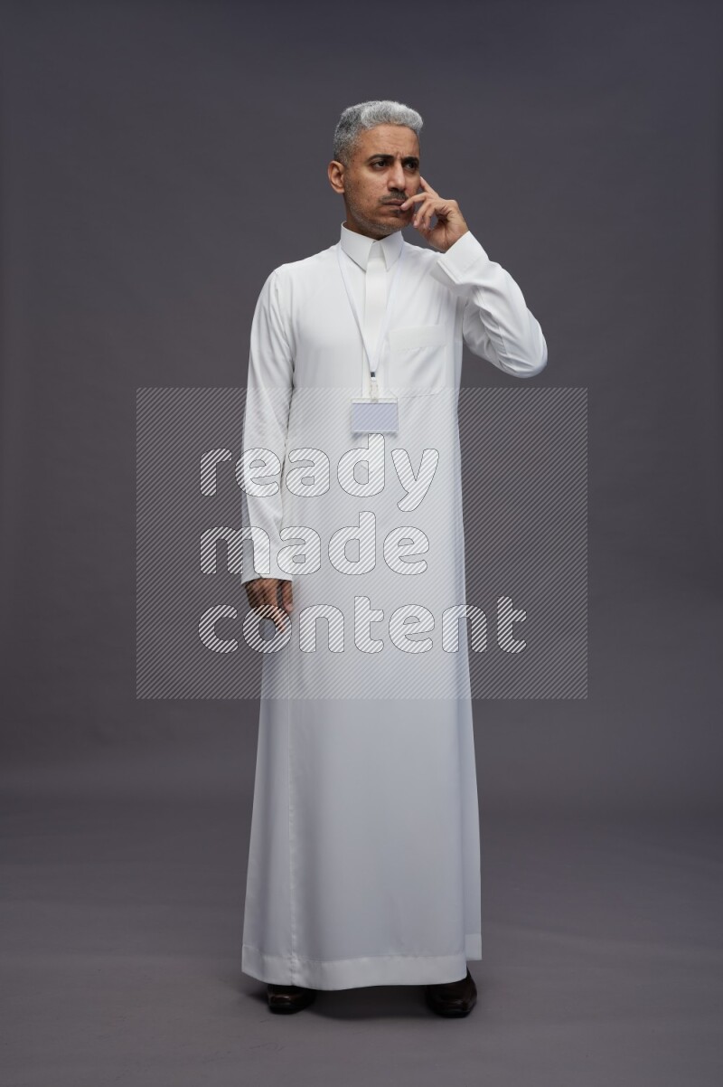Saudi man wearing thob with neck strap employee badge standing interacting with the camera on gray background