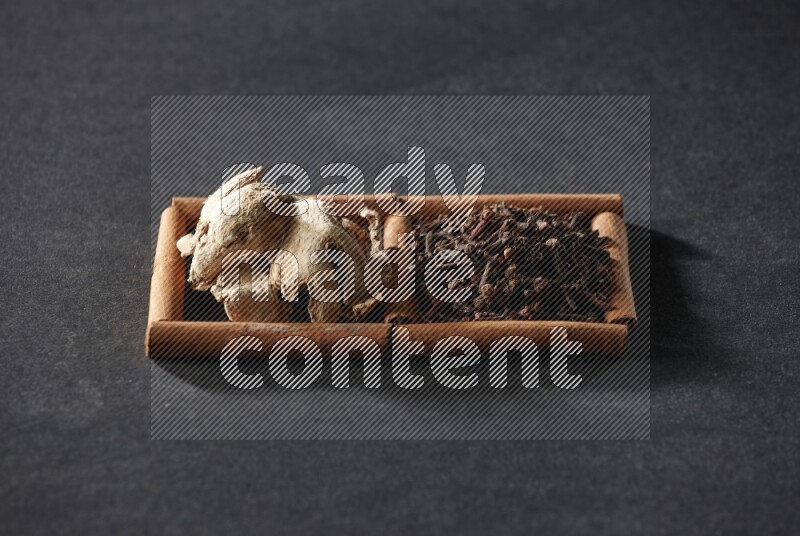 مربعان من أعواد القرفة ممتلئان بالقرنفل والزنجبيل المجفف علي خلفية سوداء