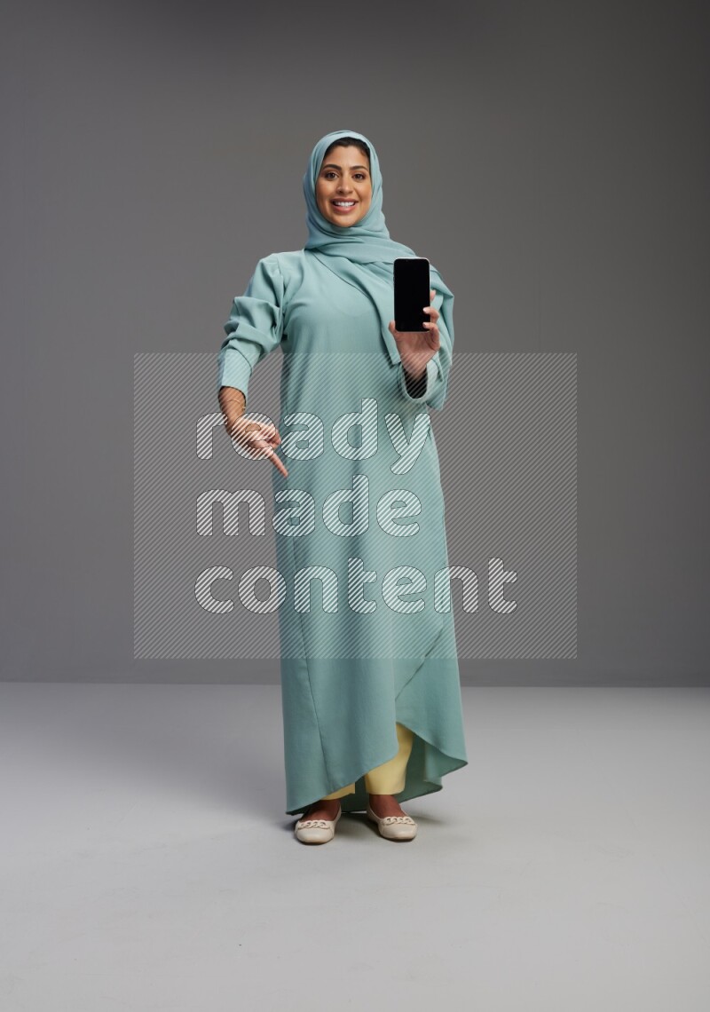 Saudi Woman wearing Abaya standing showing phone to camera on Gray background