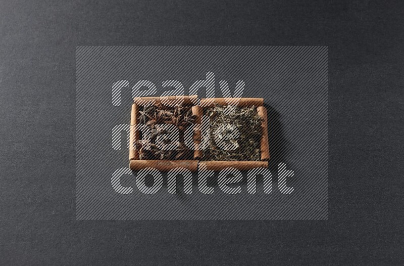 مربعان من أعواد القرفة ممتلئان باليانسون النجمي والريحان المجفف علي خلفية سوداء