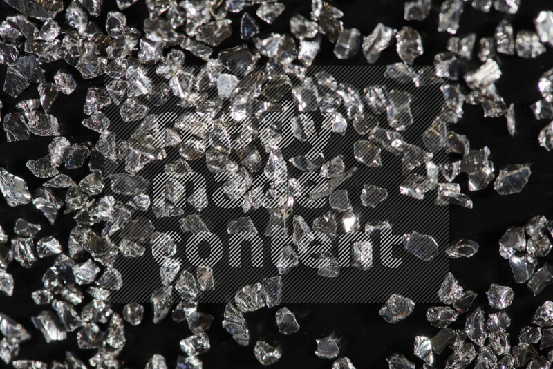 Silver shimmering fragments of glass scattered on a black background