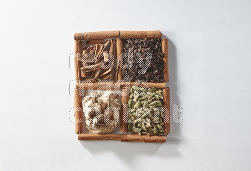 4 مربعات من أعواد القرفة ممتلئة بالهيل والقرفة والقرنفل والزنجبيل المجفف على أرضية بيضاء