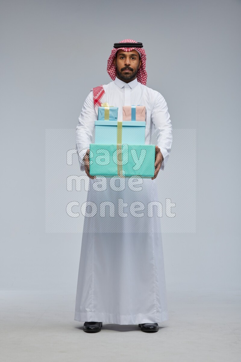 Saudi man Wearing Thob and shomag standing holding gift box on Gray background