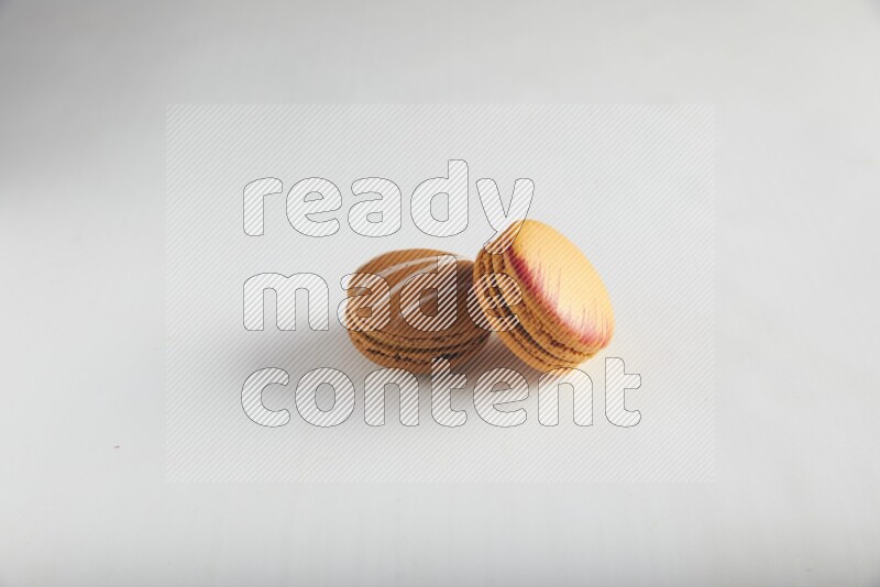45º Shot of of two assorted Brown Irish Cream, and Orange Exotic macarons on white background