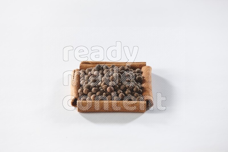 أربعة من أعواد القرفة مكونة شكل مربع بداخلها بهار الفلفل الحلو علي خلفية بيضاء