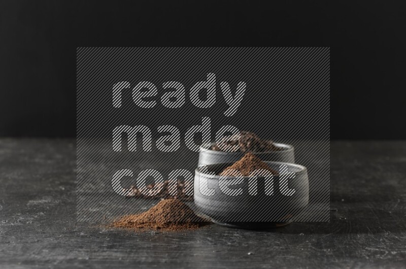 وعاءين من الفخار الأسود أحدهما ممتلئي بحبوب القرنفل والآخر ممتلئ ببودرة القرنفل على خلفية سوداء