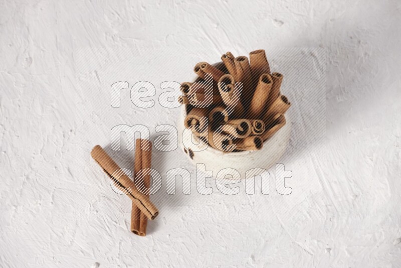 Cinnamon sticks in a beige bowl on a white background