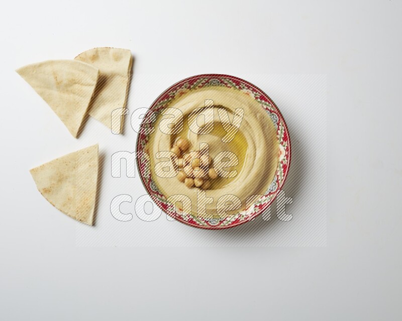 Hummus in a red plate with patterns garnished with roasted chickpeas  on a white background