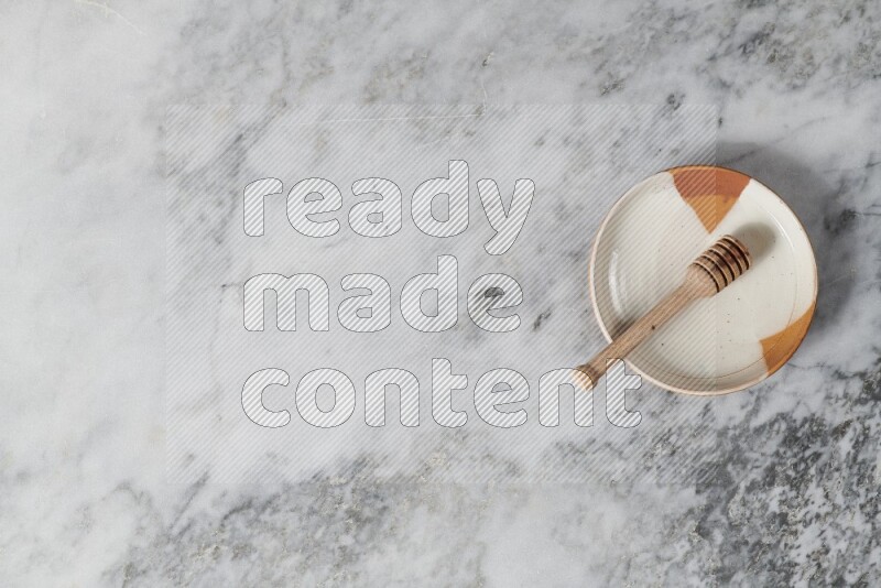 Multicolored pottery plate with wooden honey dipper in it on grey marble background