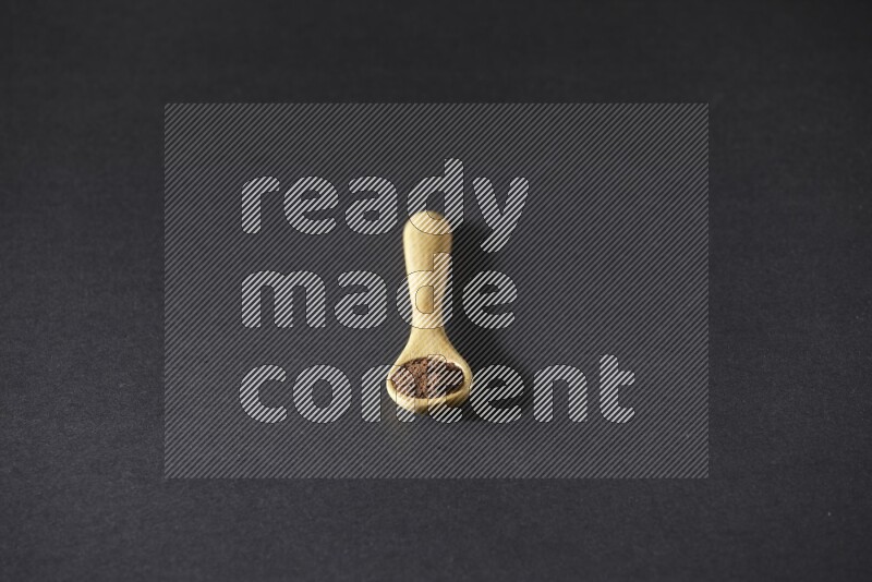 A wooden spoon full of cloves powder on a black flooring