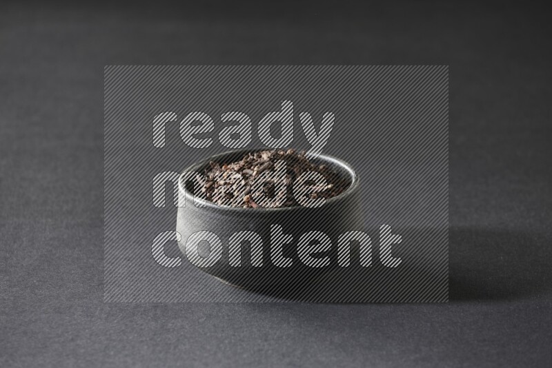 A black pottery bowl full of cloves on a black flooring