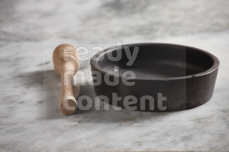 Black pottery oven plate with wooden honey dipper on the side on grey marble background