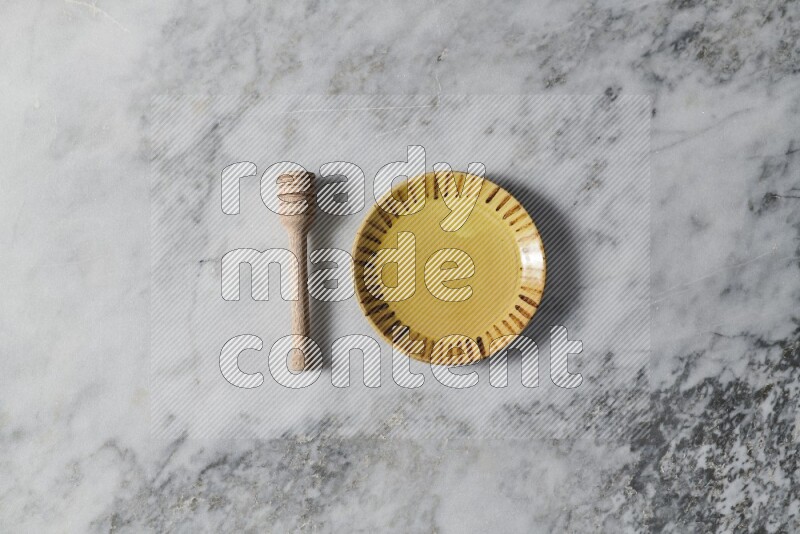 Multicolored pottery plate with wooden honey dipper on the side on grey marble background