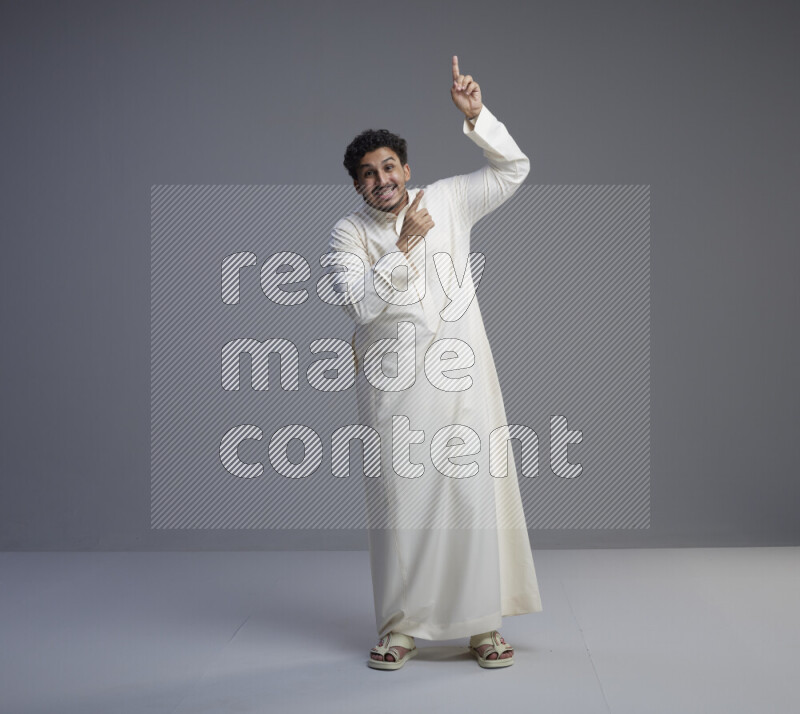 A Saudi man standing wearing thob interacting with the camera on gray background