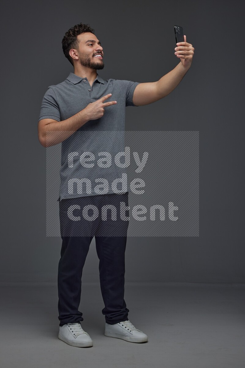 A man wearing casual and taking selfie with his phone different angles eye level on a gray background