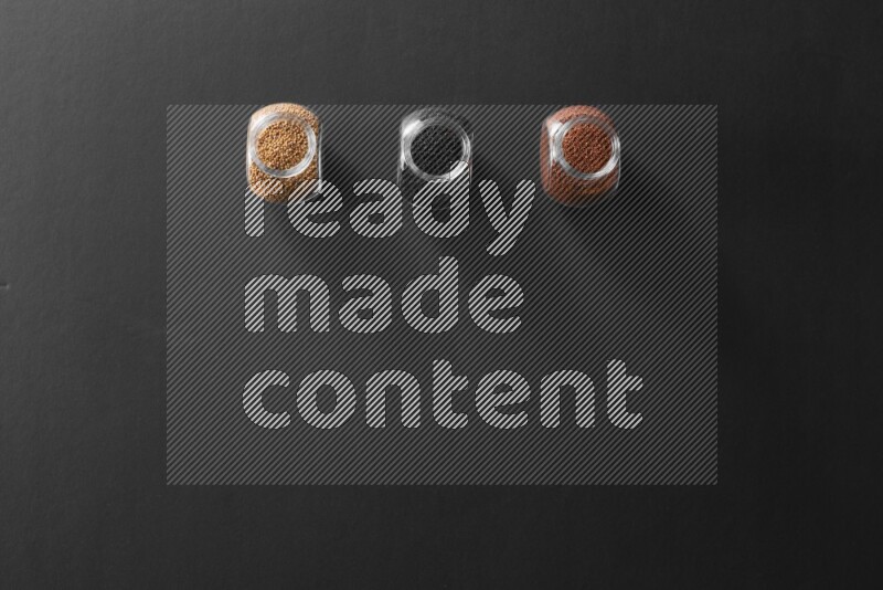 3 glass spice jars full of black seeds, mustard seeds and garden cress on black flooring