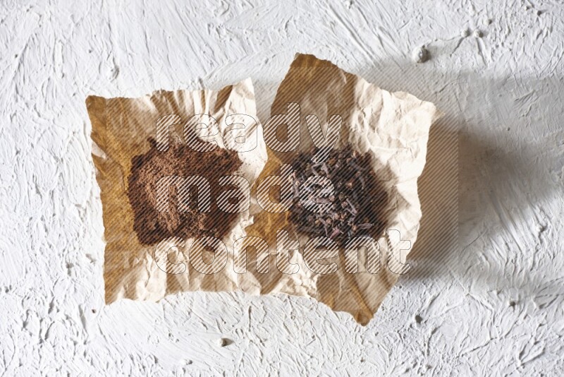 Cloves powder and cloves on 2 crumpled pieces of paper on a textured white flooring
