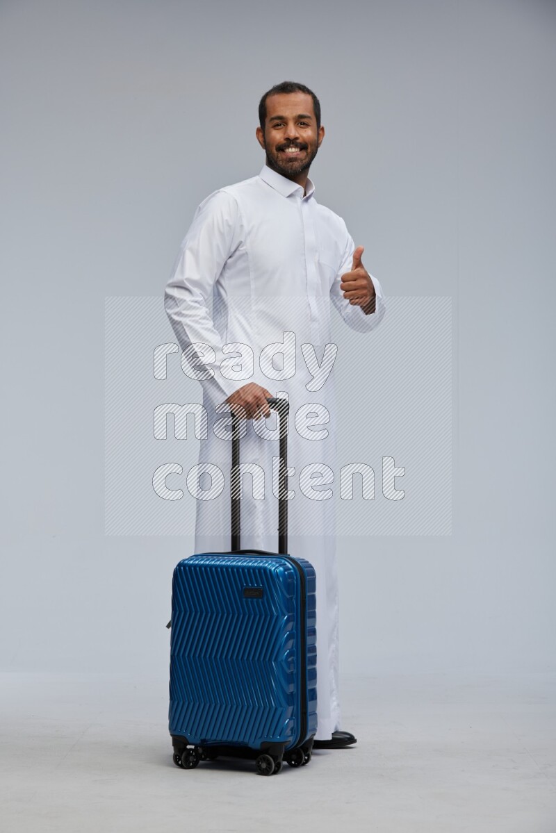 Saudi man wearing thob standing holding Travel bag on Gray background