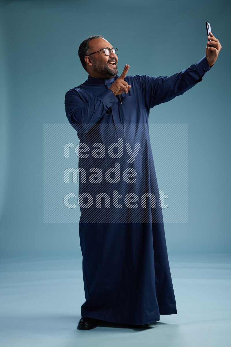 Saudi Man without shimag Standing taking selfie on blue background
