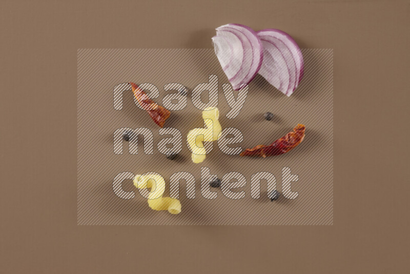 Raw pasta with different ingredients such as cherry tomatoes, garlic, onions, red chilis, black pepper, white pepper, bay laurel leaves, rosemary and cardamom on beige background