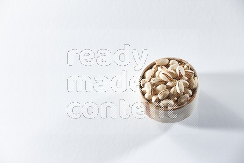A beige ceramic bowl full of pistachios on a white background in different angles